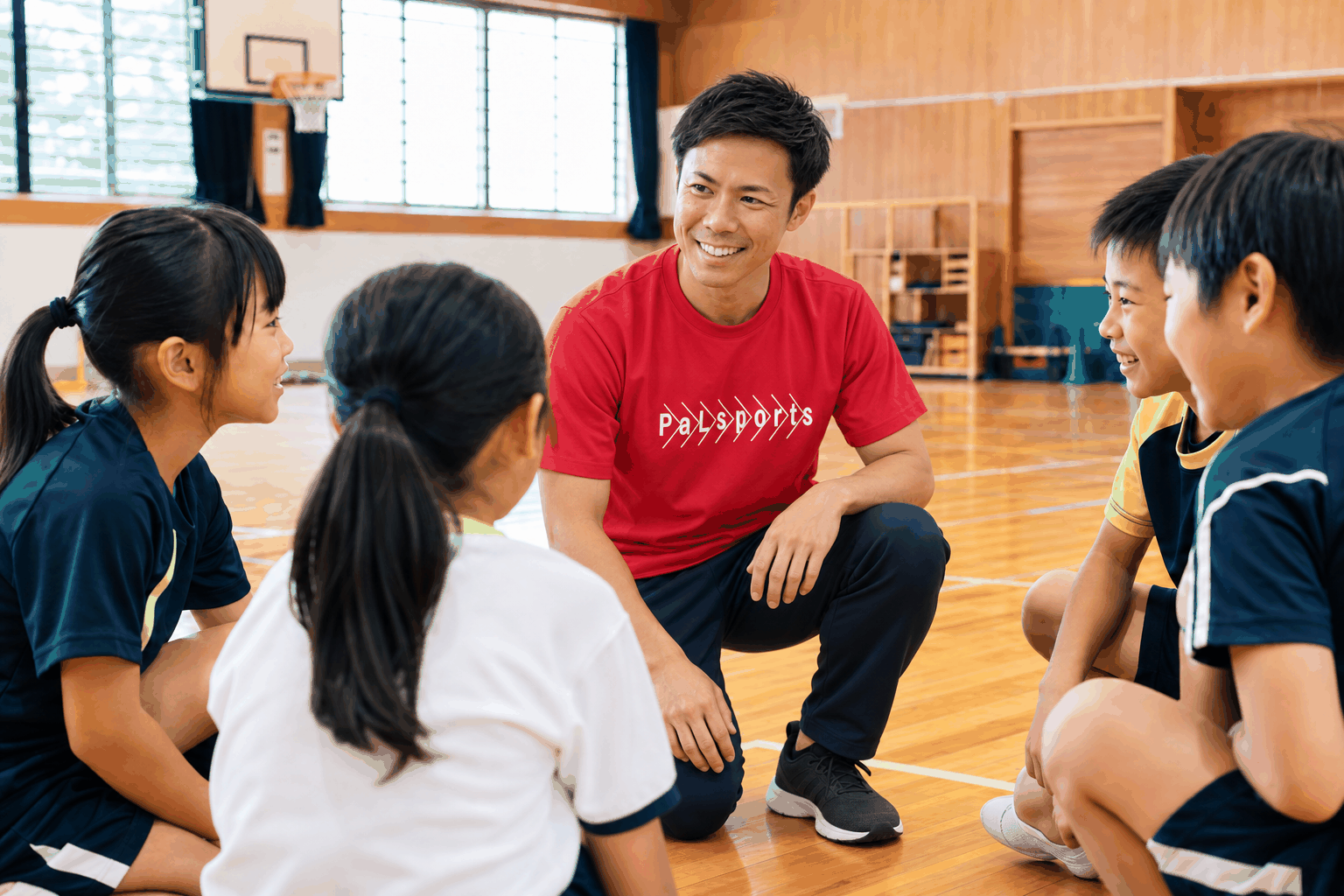 子どもたちと同じ目線で笑顔で話すコーチのイメージ